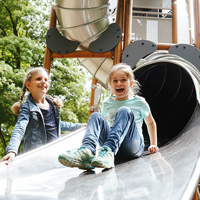 Ältere Kinder rutschen durch eine große Röhrenrutsche und lächeln bei der Abfahrt. 